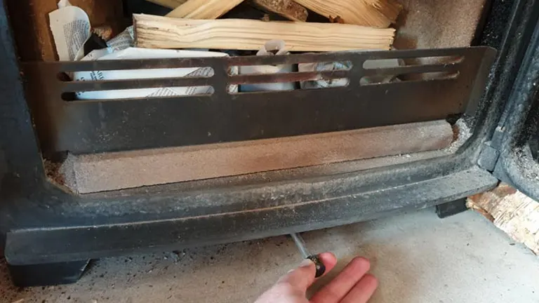 Fireplace grate with a hand holding a small tool.