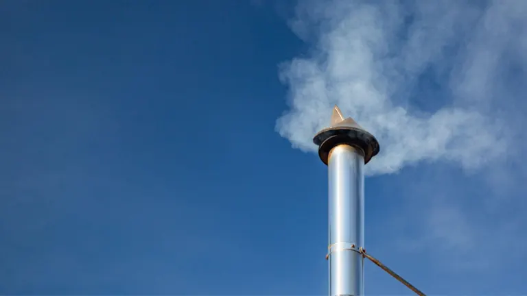 Chimney with smoke against a clear blue sky