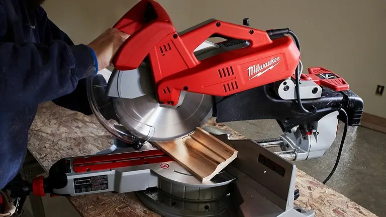 Person in blue shirt using a red Milwaukee 6955-20 12” Dual-Bevel Sliding Compound Miter Saw to cut wood on a workbench