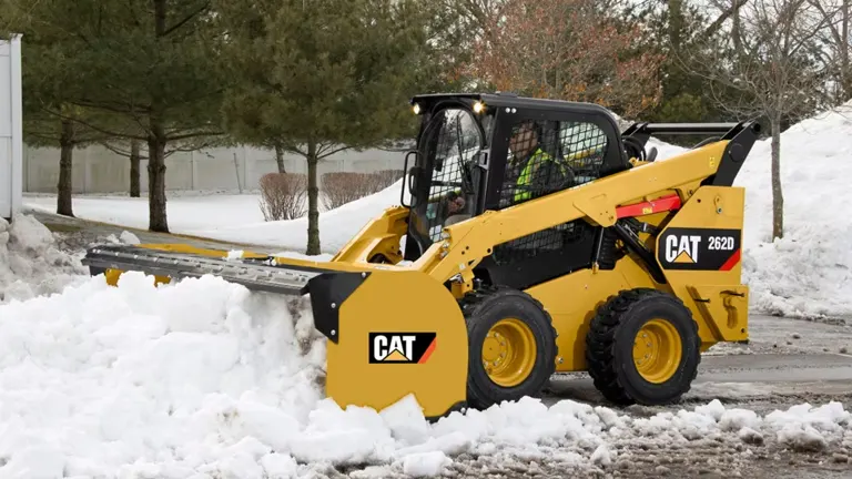 Yellow CAT 262D skid steer loader clearing snow from a road.