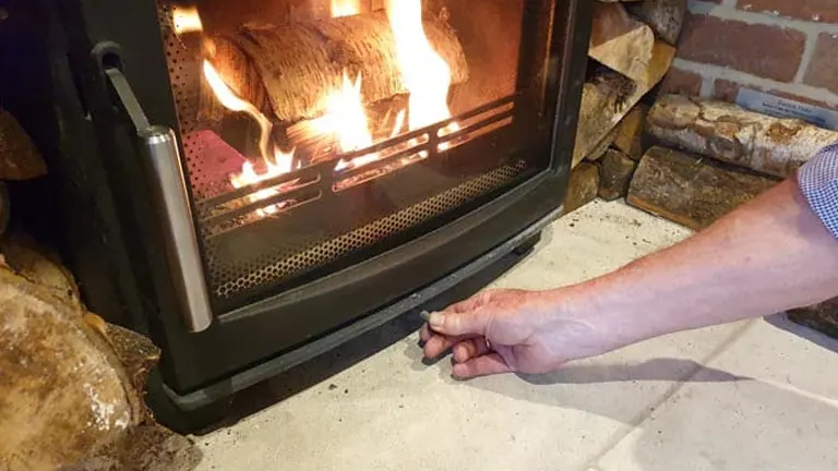 Hand adjusting the handle of a fireplace with a fire burning inside.