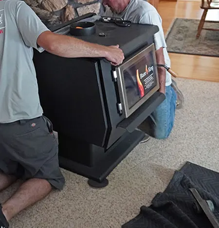 Two people moving a black wood stove