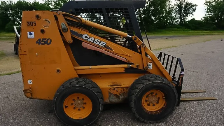 Orange Case 450 skid steer loader with a bucket attachment parked on a road with trees in the background.