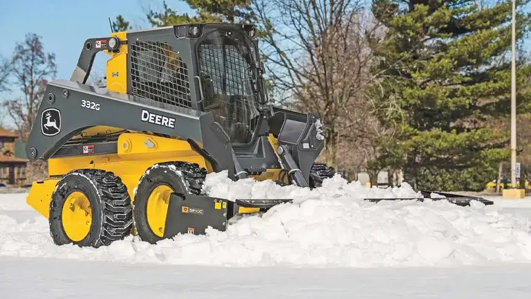 Yellow John Deere skid steer loader clearing snow from a parking lot.
