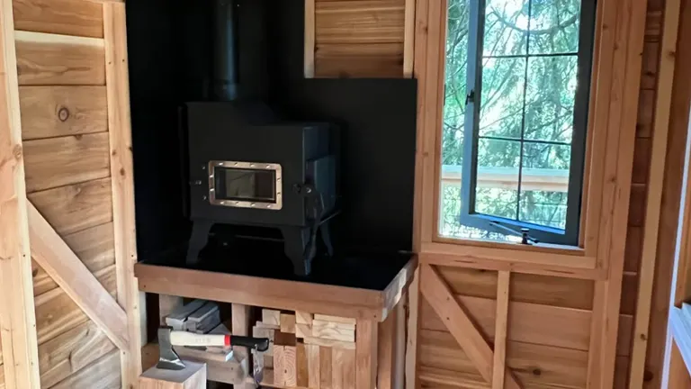 Wood stove in a wooden cabin with a window view of trees.