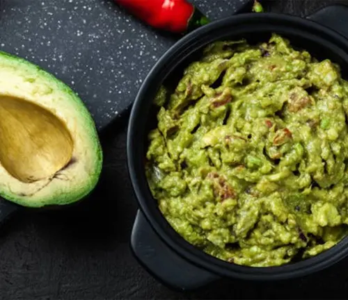Bowl of guacamole with halved Hass avocado and red chili pepper