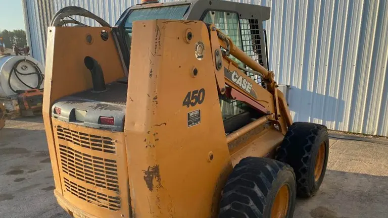 Yellow Case 450 skid steer loader parked in front of a corrugated metal building.