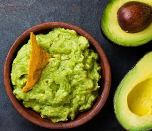 Bowl of guacamole with tortilla chip and halved avocado