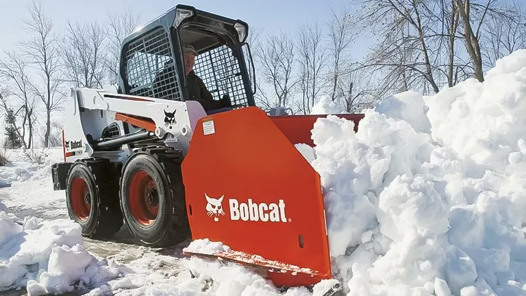 White Bobcat skid-steer loader clearing snow with a red bucket.