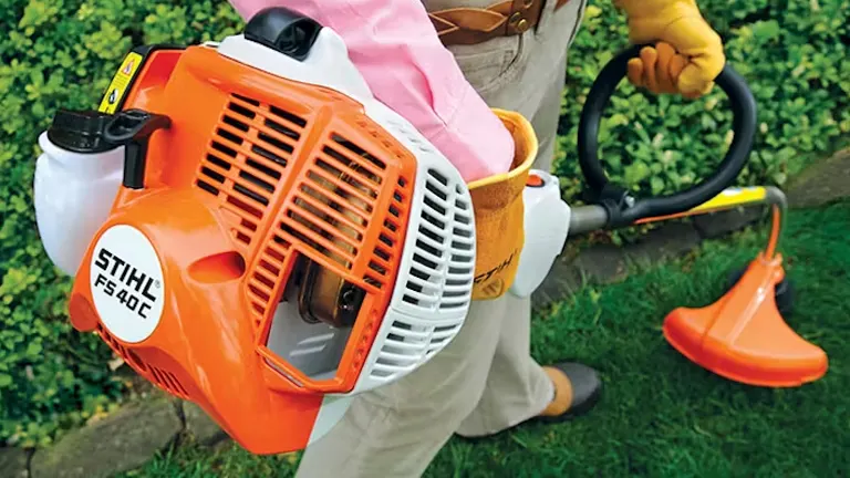 Person in gray outfit using an orange and white STIHL FS 40 C-E Trimmer in a garden