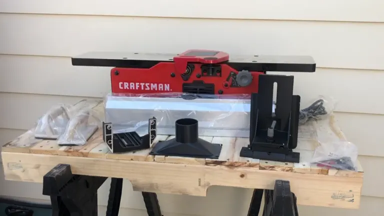 Red Craftsman wood jointer on wooden workbench with accessories.