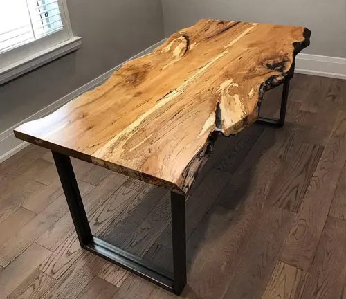 Wooden table with a natural edge and black metal legs in a room with hardwood flooring and a window