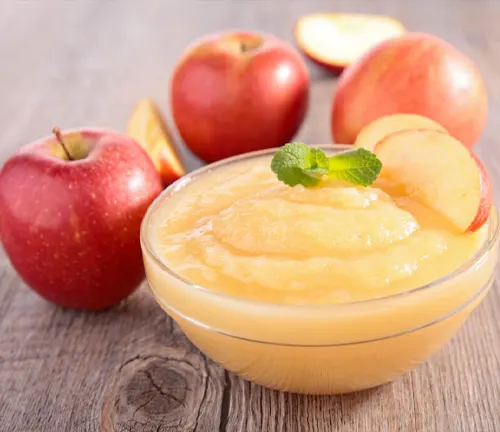 Bowl of applesauce with fresh apples on a wooden table.