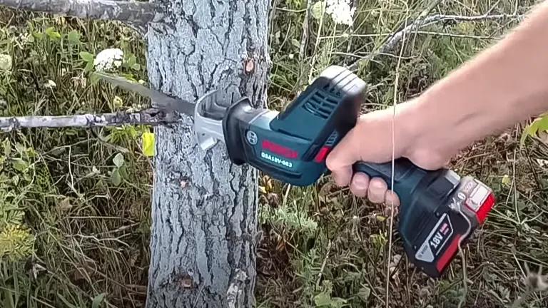 A person using a BOSCH GSA18V-083B 18V Compact Reciprocating Saw to cut a tree trunk
