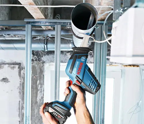 A person using a BOSCH GSA18V-083B 18V Compact Reciprocating Saw to cut through a pipe in a construction site