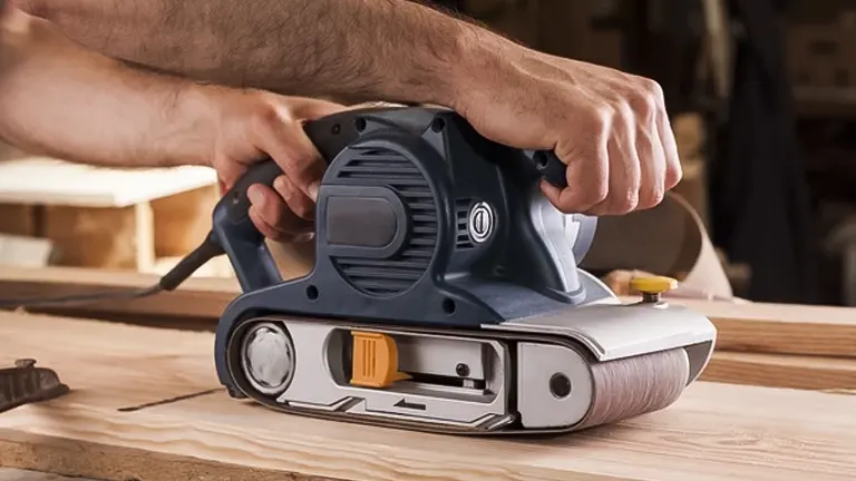 Person using a blue and gray belt sander on a wooden surface