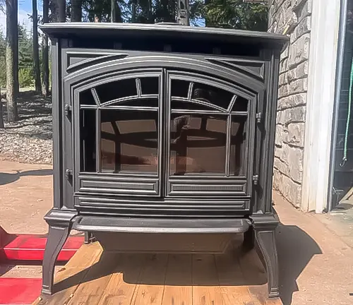 Black wood-burning stove on a wooden deck with a stone wall.