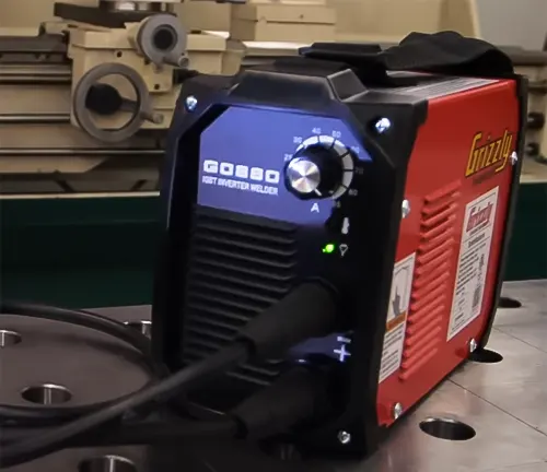 Grizzly G0880 85A Stick Welder on a workbench with blurred tools and machinery in the background.