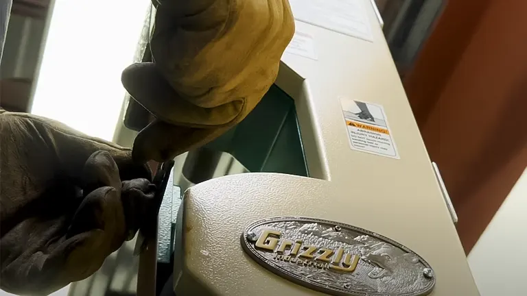 Close-up of a Grizzly 2” x 48" 2-Wheel Belt Grinder/Sander with a person’s gloved hand operating it
