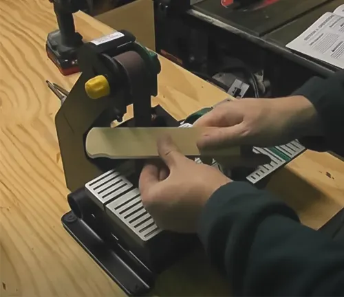 A person using a Grizzly H7760 Combo Belt Sander/Grinder on a wooden workbench in a workshop