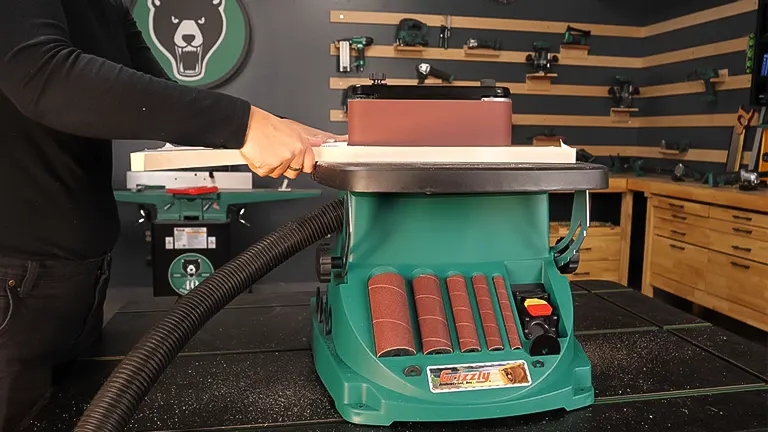 Person’s hand on a green Grizzly T27417 Oscillating Edge Belt and Spindle Sander on a workbench