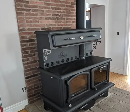 Black J. A. ROBY wood burning cook-stove with brick chimney in room with wooden flooring