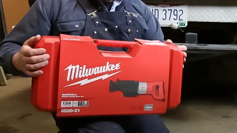 Person in blue uniform holding a red Milwaukee T25741 - 13 Amp Sawzall Reciprocating Saw case in a workshop