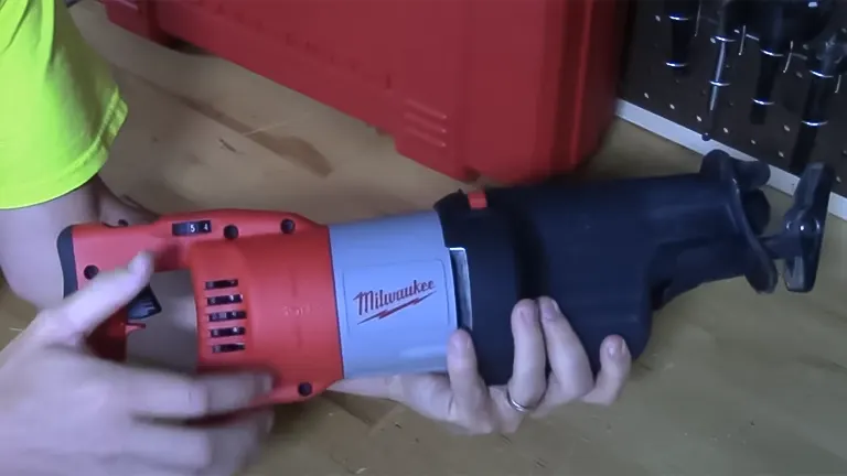 Person holding a red and gray Milwaukee T25741 - 13 Amp Sawzall Reciprocating Saw in front of a red toolbox in a workshop