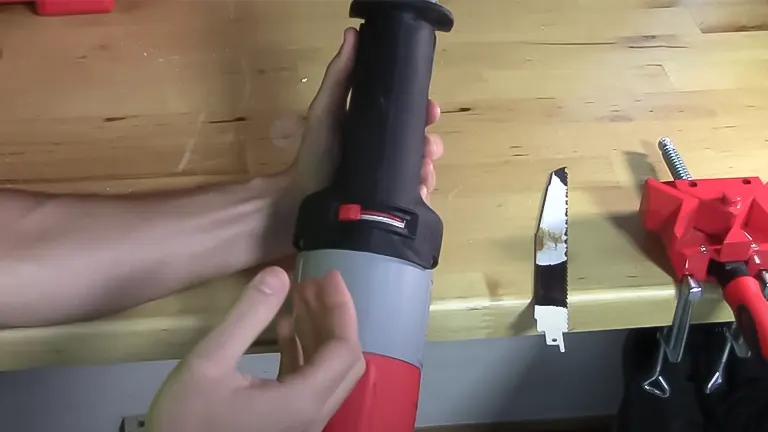 Person holding a red and black Milwaukee T25741 - 13 Amp Sawzall Reciprocating Saw with a gray handle on a wooden workbench