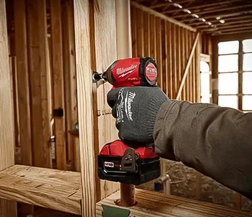 Hand holding a red and black power drill at a wooden construction site.