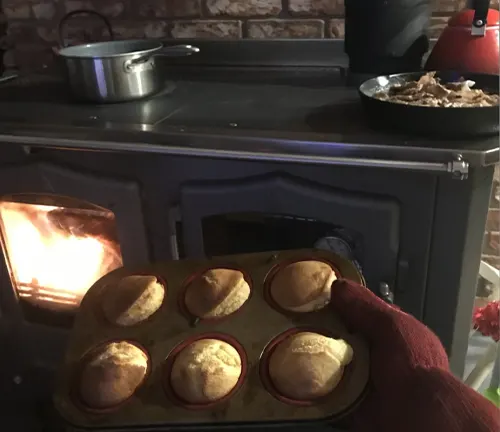 Tray of freshly baked muffins being taken out of a wood-fired oven in a kitchen.