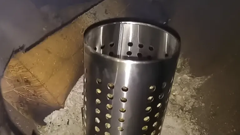 Metal cylinder with holes on pile of ash.