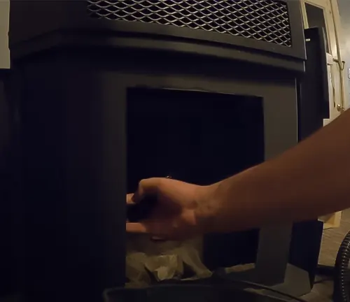 Hand opening a black pellet stove door.
