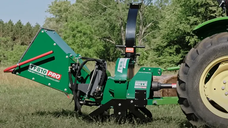 Green Woodland Mills TF810 PRO PTO Wood Chipper with ‘TURBINE TECHNOLOGY’ label, attached to a tractor in a sunny, grassy field