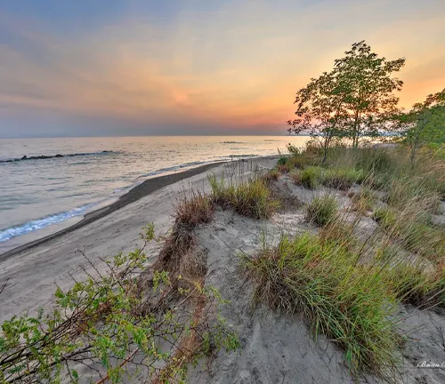 Sunset over the serene beaches of Presque Isle State Park, highlighting the gentle waves, sandy shores, and lush greenery