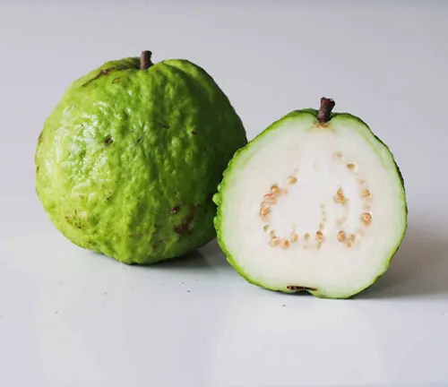A whole and a halved Psidium guajava showing the green outer skin and white inner flesh with seeds