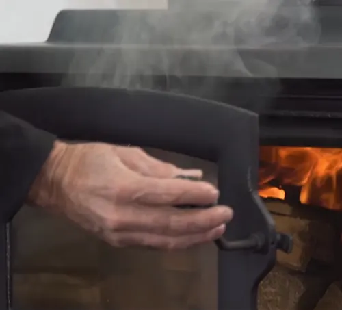 Hand opening the door of a smoking wood stove