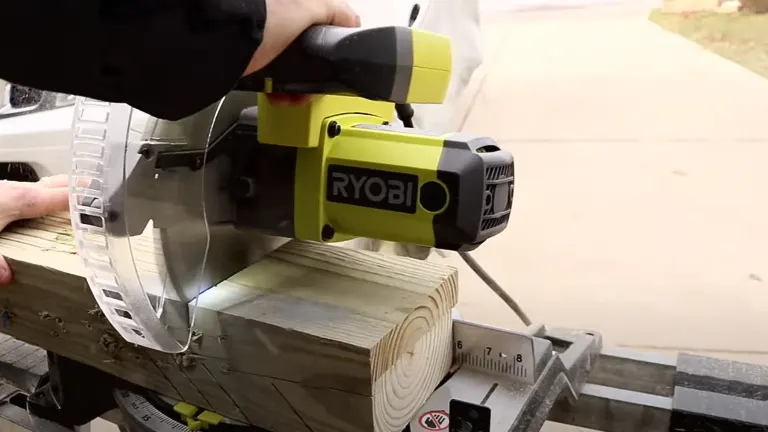 Green and black Ryobi 10-inch sliding compound miter saw in use on a wooden plank in a workshop