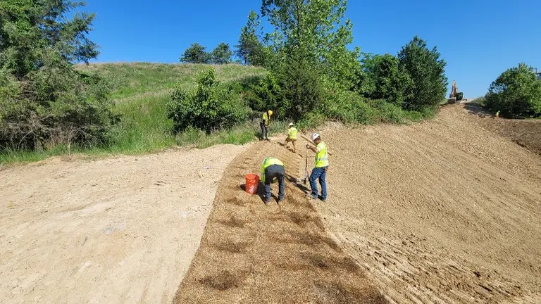 workers in safety vests and helmets applying erosion control measures on a sloped terrain