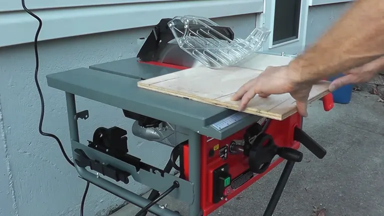 Person’s hands operating a red and grey Craftsman 10-inch portable table saw outside, next to a building
