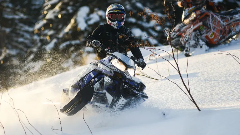 A person riding a snowmobile at high speed in the snowy terrain of White Mountain National Forest