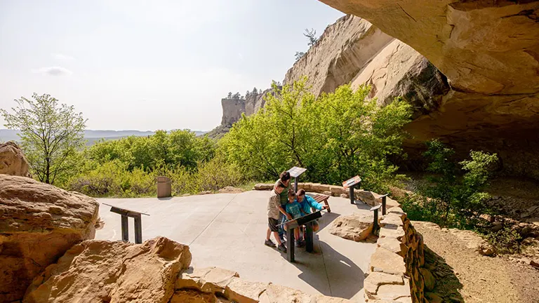 Visitors exploring Pictograph Cave State Park under an overhanging rock formation