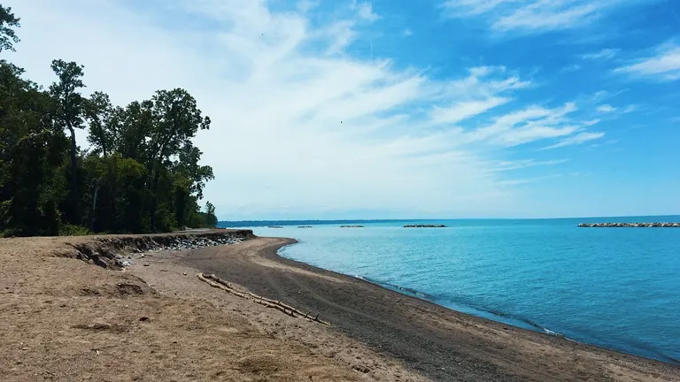 Sunny day at Presque Isle State Park with a clear blue sky, calm lake, and sandy shoreline surrounded by green trees
