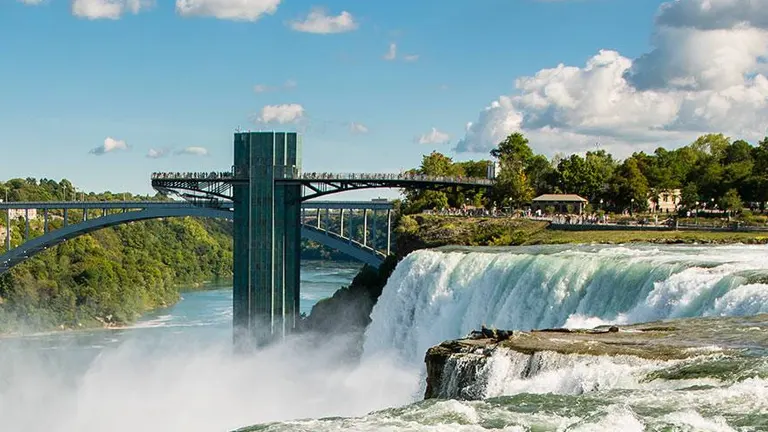 Scenic view of Niagara Falls with a bridge overhead and lush greenery surrounding