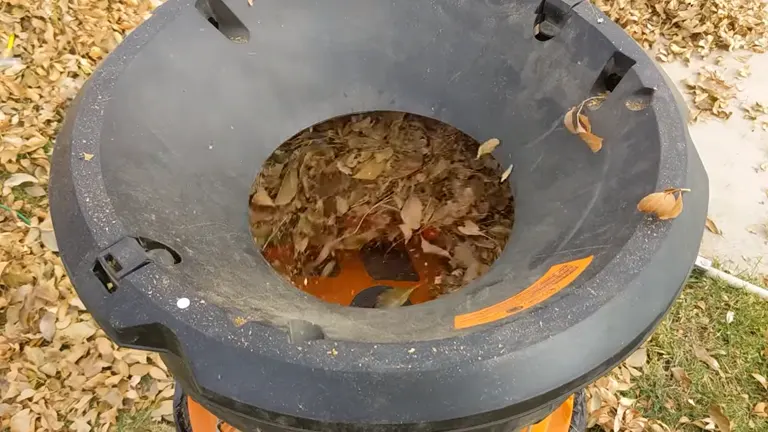 Worx WG430 Electric Leaf Mulcher outdoors, filled with dry leaves, surrounded by scattered leaves on the ground