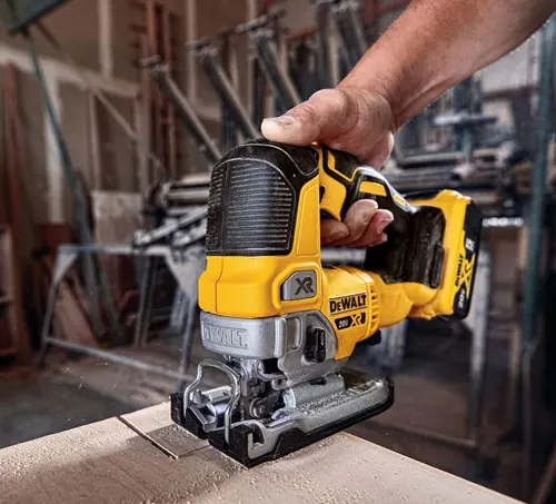 A person using a yellow and black DeWalt reciprocating saw to cut through a wooden board in a workshop