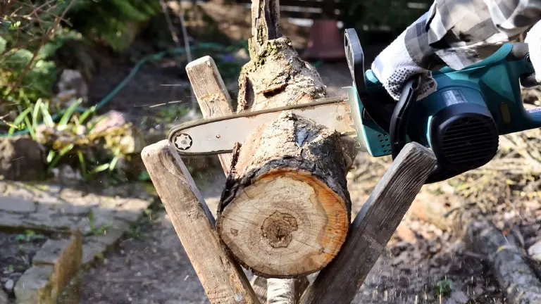 A person using a chainsaw to cut a log secured on a wooden stand