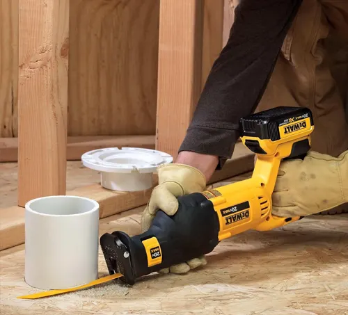 A person using a yellow reciprocating saw to cut through a white PVC pipe