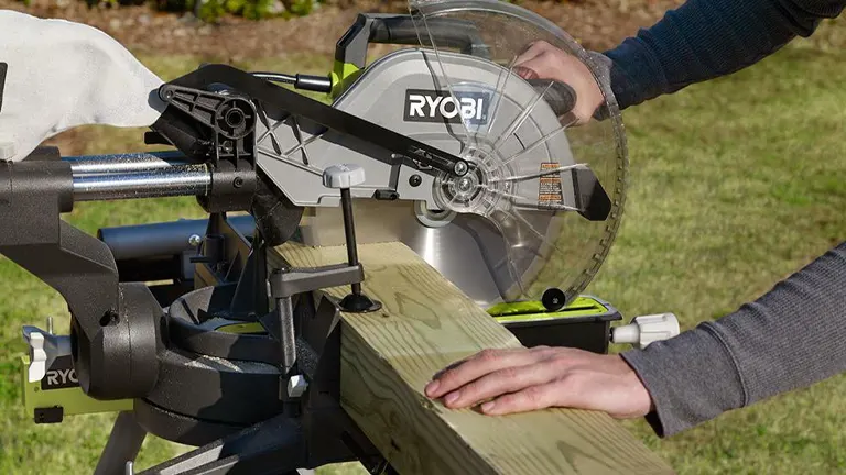 A person using a Ryobi 12” Sliding Compound Milter Saw to cut a wooden plank in a garden setting