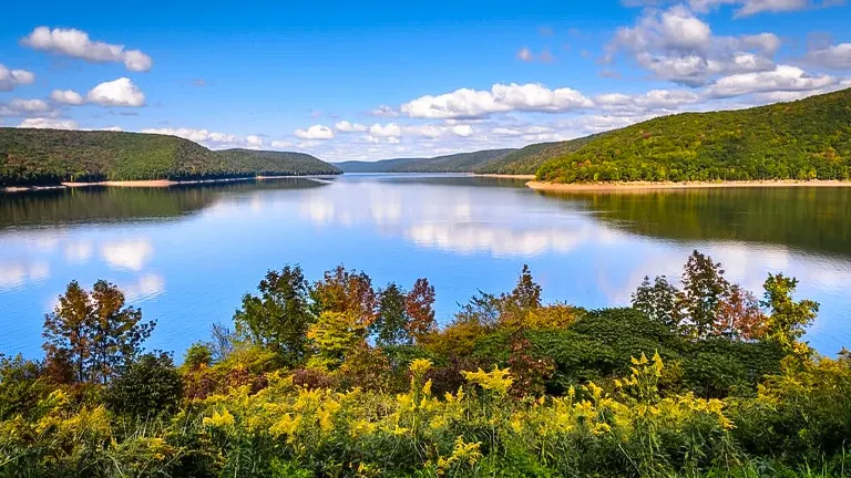 Serene view of Allegheny National Forest with a calm lake reflecting the clear sky, surrounded by lush hills